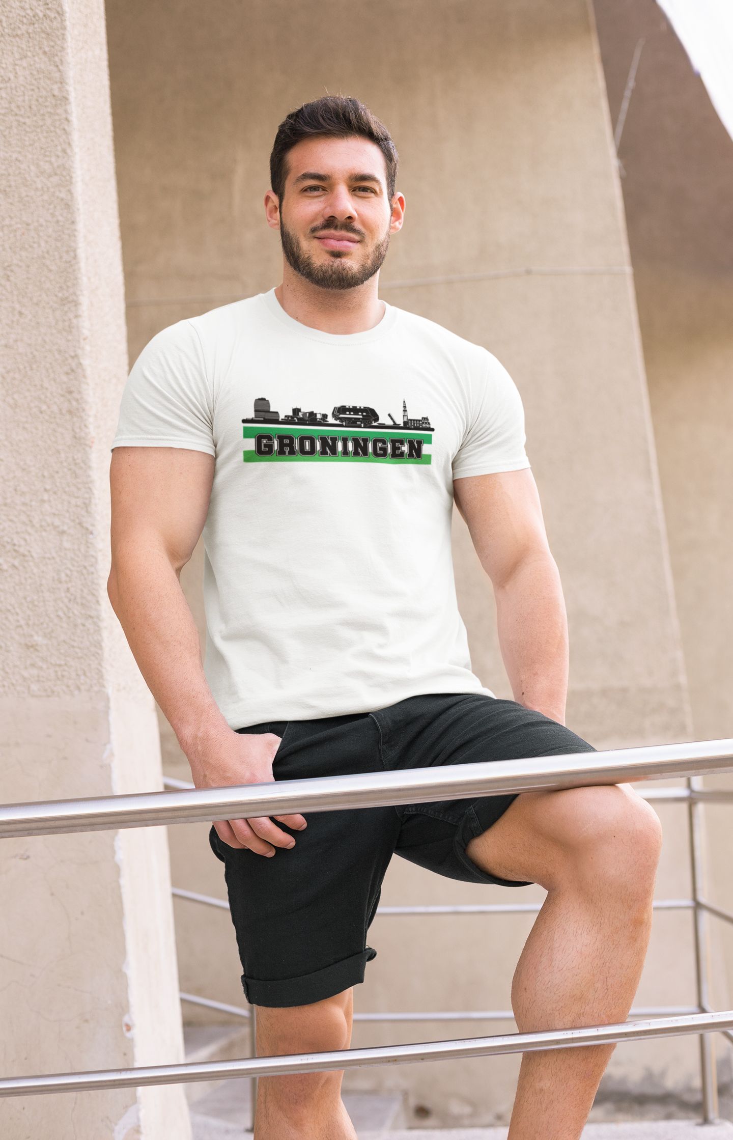 Man draagt T-shirt met skyline van Groningen en groene tekst "Groningen", verkrijgbaar in meerdere kleuren.